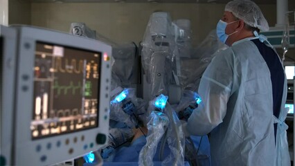 Medical equipment and monitors in background. Robotic surgery in sterile environment. Surgeon controls robot with multiple arms and performs surgical procedure. - Powered by Adobe