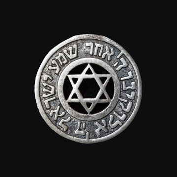 Old silver medallion with the Star of David and the text of the prayer "Hear, oh Israel, the Lord is our God, the Lord is one" on a black velvet background