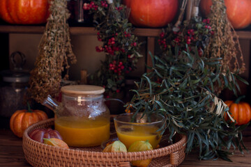 yellow tea with sea buckthorn berries in a glass teapot. Decorated with physalis and autumn pumpkins, dried herbs for winter in the background