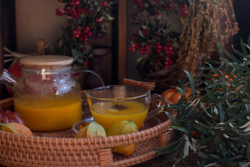 yellow tea with sea buckthorn berries in a glass teapot. Decorated with physalis and autumn pumpkins, dried herbs for winter in the background