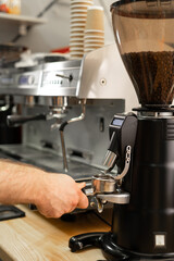 Close-up of the coffee grinder machine in a coffee shop. Barista grinding roasted coffee beans from a professional electric grinder. Cafe service