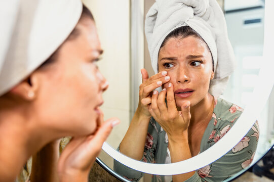 Worried woman looking in bathroom mirror worried about wrinkles and aging.