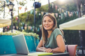 Beautiful woman freelancer planning project doing remote job via laptop computer in the street cafe. Charming female caucasian freelancer sitting in a street cafe with her notebook.