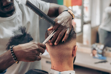 Crop black barber cutting hair of client with scissors