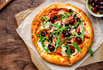 Homemade Pizza with sausage, cheese, mushrooms, olives, tomato sauce and arugula, rustic wooden table background, top view