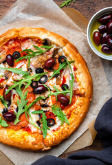 Homemade Pizza with sausage, cheese, mushrooms, olives, tomato sauce and arugula, rustic wooden table background, top view