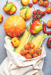 Autumn vegetables and fruits from farm market in beige textile eco-friendly bag, healthy vegan food, gray background, top view
