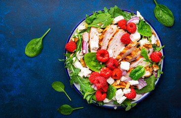 Gourmet salad with raspberries, grilled chicken, feta cheese, red onion, walnuts, spinach and mixed herbs, blue table background, top view