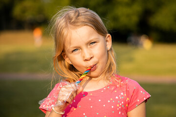 Smiling little girl child with colorful lolipop in the park