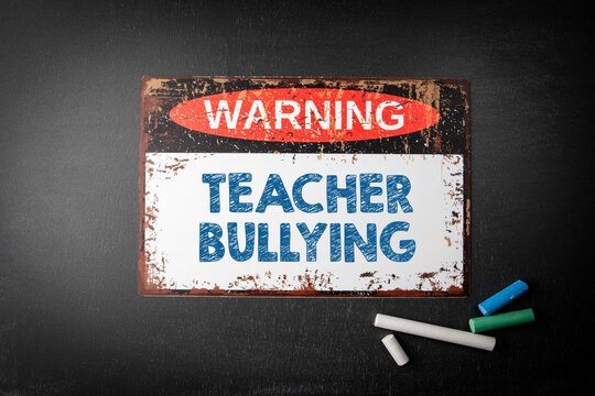 Teacher Bullying. Metal warning sign and colored pieces of chalk on a dark chalkboard background