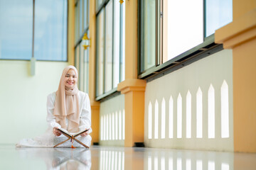 The image of an Asian Muslim woman in the Islamic religion in hijab in cream color. reading the...