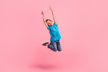 Full length photo of impressed cheerful small boy wear blue t-shirt rising hands arms jumping high...