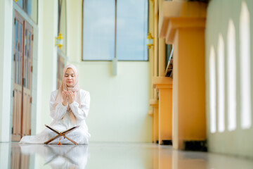 The image of an Asian Muslim woman in the Islamic religion in hijab in cream color. reading the...