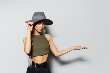 Studio portrait of beautiful blonde girl holding palms on copy space background of white. Wearing grey hat.