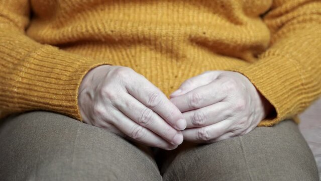 Mature woman touches trembling wrinkled hands in unsure manner. Lady trying to explain mental health problems to professional nurse at home