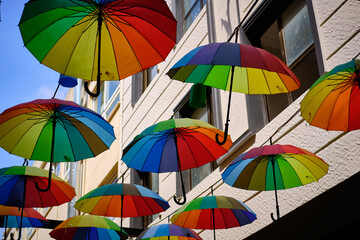 Fototapeta na wymiar Lots of rainbow-colored umbrellas hanging above street. Decoration of streets made of umbrellas
