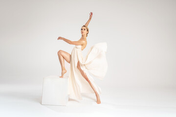 Young female blonde dancer wearing elegant dress dancing over grey light studio background. Copy space.