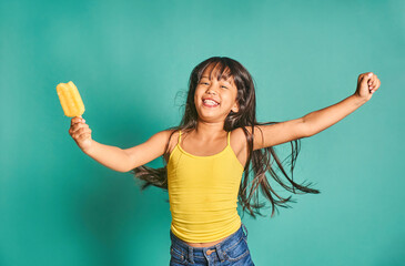 Happy ethnic girl child standing with popsicle in hand against turquoise backdrop