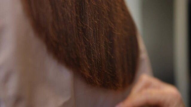 Close-up brunette hair with female hand combing haircut leaving in slow motion. Unrecognizable Caucasian hairdresser styling hairdo of client in beauty salon indoors