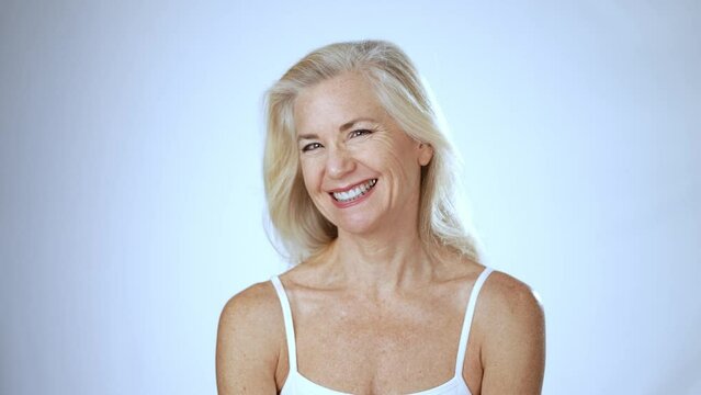 Portrait of mature woman touching face, spa concept of beauty, looking and smiling at camera, studio white background