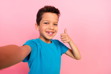 Photo of cool confident small boy wear blue t-shirt recording video vlog showing thumb up isolated pink color background