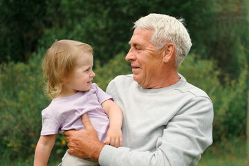 Grandfather and grandchild baby have fun during walk In Park. Happy family. Old man grandpa hugging 2 years child girl at summer day. Smiling Senior male spending time with his granddaughter together