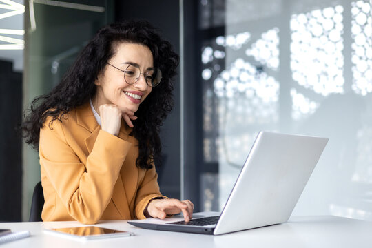 Happy and smiling hispanic businesswoman typing on laptop, office worker with curly hair and glasses happy with achievement results, at work inside office building. .