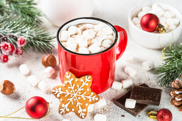 Hot chocolate with marshmallow and gingerbread cookies and holiday decorations at white table.