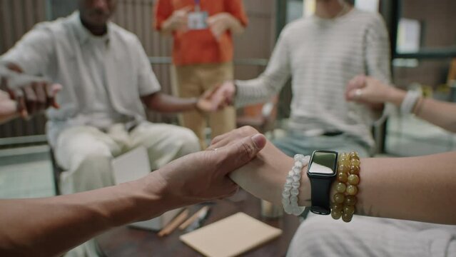 Cropped selective focus shot of people holding hands while sitting in circle on group therapy session