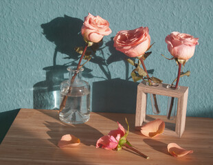 Pink roses in glass vase on blue background. Pink flowers on blue textured wall. Minimalist floral concept. Flowers bouquet in glass vase. Romantic, love. Vintage aesthetic. Rose petals on wood table.
