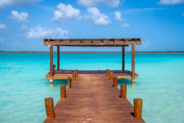 A wooden pier heading toward the horizon on a crystal clear blue water in Bacalar, Mexico