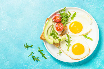 Breakfast. Fried egg, toast with salmon and avocado and fresh salad. Healthy food. Top view with copy space at blue table.