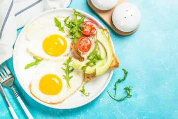 Breakfast. Fried egg, toast with white cheese and avocado and fresh salad. Healthy food. Top view with copy space at blue table.