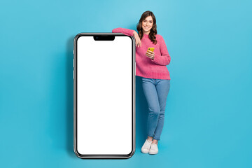 Full length photo cadre of young charming attractive girl wear pink sweater jeans hold phone huge touchscreen menu isolated on blue color background