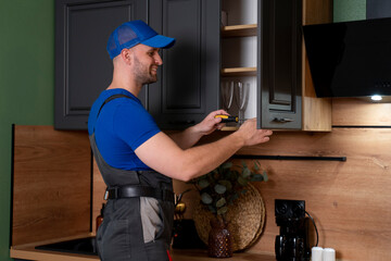 Repairman in overalls repairing cabinet hinge in kitchen. Male hand adjusting a mechanism....