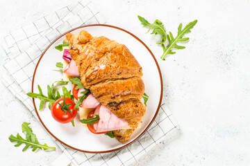 Croissant sandwich with ham, cheese and fresh salad in white plate. Top view with copy space on white stone table.