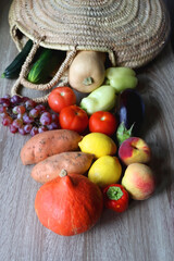 Round straw bag with seasonal fruit and vegetable on wooden background. Late summer or early autumn. Selective focus.