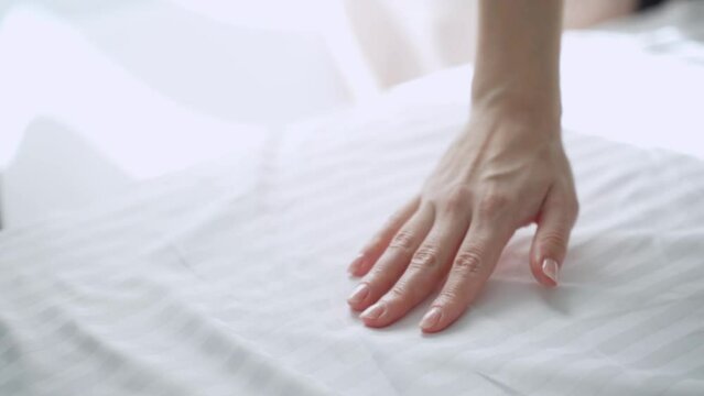 The tenderness and softness of striped satin bed linen - a woman touches a white sheet with her hand