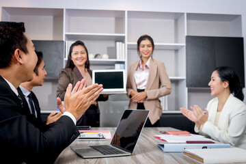 Businesspeople discussing at conference office desk, business team clapping hands to admire compliment during successful businesswomen showing laptop computer for presentation at group board meeting.