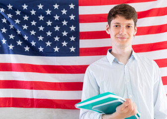 Young guy with notebooks posing against background of USA flag