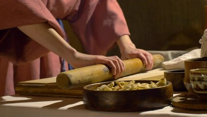 A woman rolls out the dough with a rolling pin on a wooden cutting board. R0lling out dough.