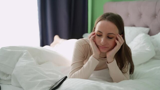 Frustrated young woman lying on the bed and looking at the phone while waiting for a message about a mobile call feels anxious, sad, offended, jealous.