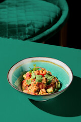 Diagonal composition of salmon tartare with mango-chili sauce in a ceramic bowl. Chair in the background. Asian restaurant, green backdrop. Stark shadows. Minimalism