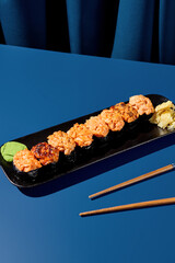 Closeup view of a spicy sushi set - baked gunkans on a black plate against a deep blue curtain backdrop. Ideal for an Asian menu.