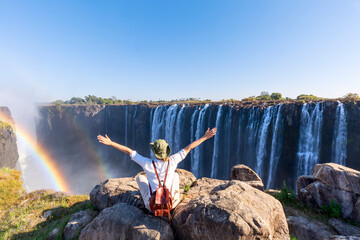 Woman sitting on the top of a rock enjoying the Victoria Falls -  Zimbabwe - obrazy, fototapety, plakaty