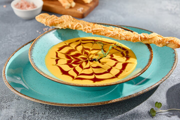 A closeup horizontal view of a bowl of creamy pumpkin soup with crostini. The texture of the soup and the gray concrete background create a feast for the eyes