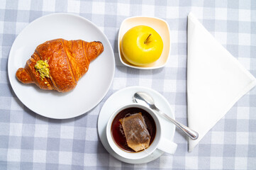 Breakfast, with brioche on a white plate, cup of tea, and an apple.