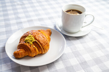 Breakfast, with brioche on a white plate, cup of tea, and an apple.