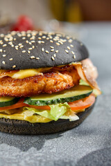 Macro vertical image capturing intricate details of a chicken and bacon burger on a black bun. The gray concrete background features harsh, aesthetic shadows