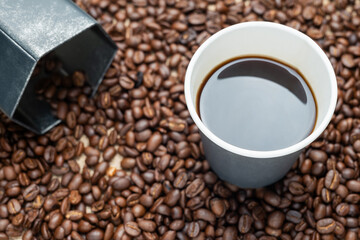 Black coffee in gray paper cup placed on the pile of coffee beans with hexagon container made of galvanized iron